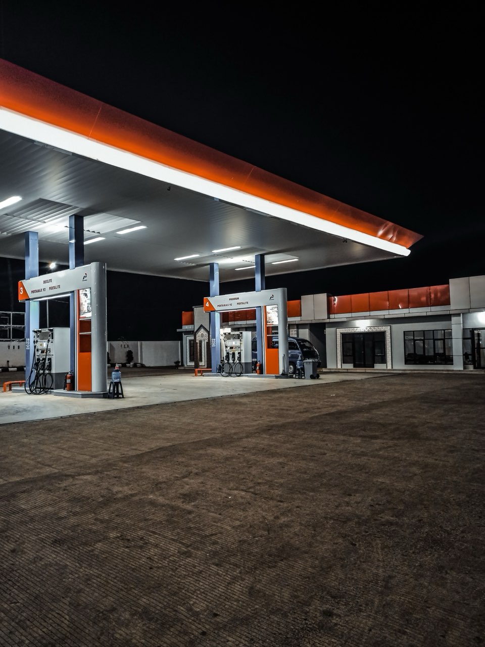 Distributore carburante notturno con pompe arancio illuminate — benzina 1.885 euro gasolio quasi 2 euro conflitto Iran-USA